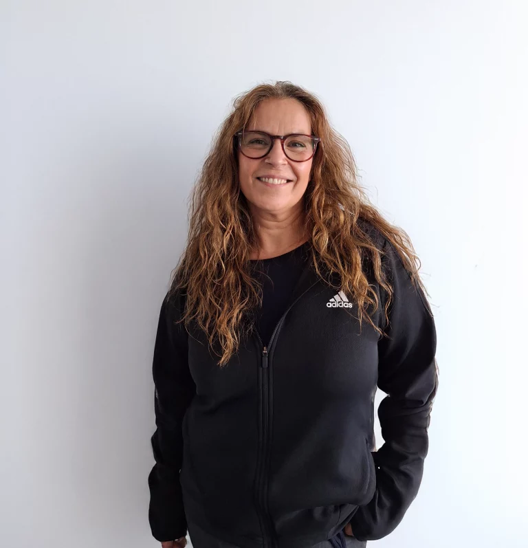Frau mit langen blonden Haaren in einem schwarzen Sweatshirt trägt eine Brille und steht vor einer neutralen Wand.
