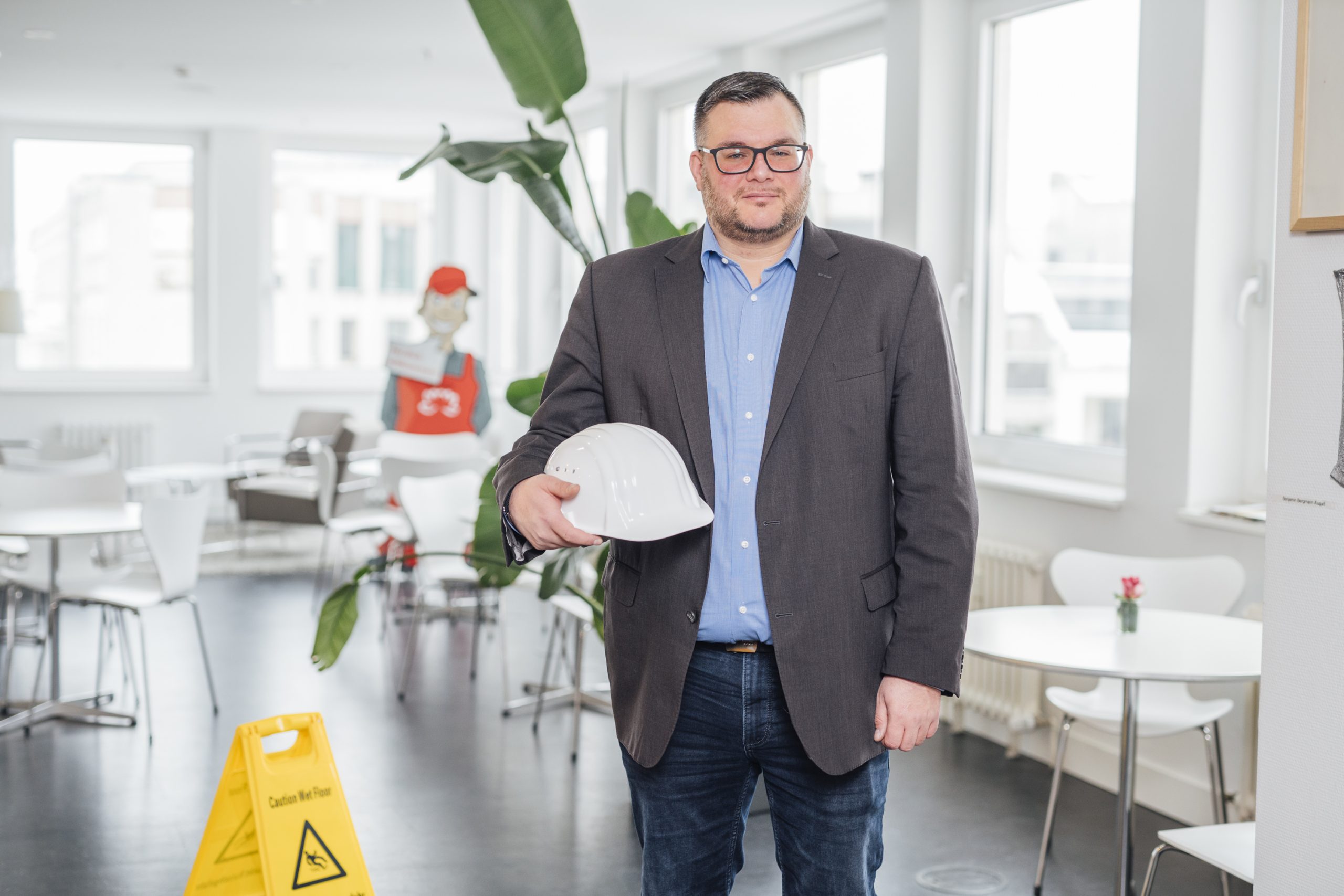 GRG-Mitarbeiter in Businesskleidung hält einen weißen Schutzhelm in einer modernen, hellen Büro- und Schulungsumgebung.
