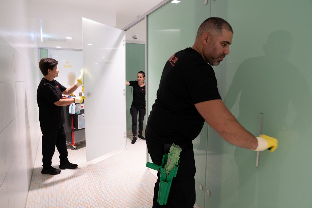 Drei GRG-Mitarbeitende in schwarzer Arbeitskleidung, zwei Frauen und ein Mann, bei der hygienischen Badreinigung mit professioneller Schutzausrüstung.