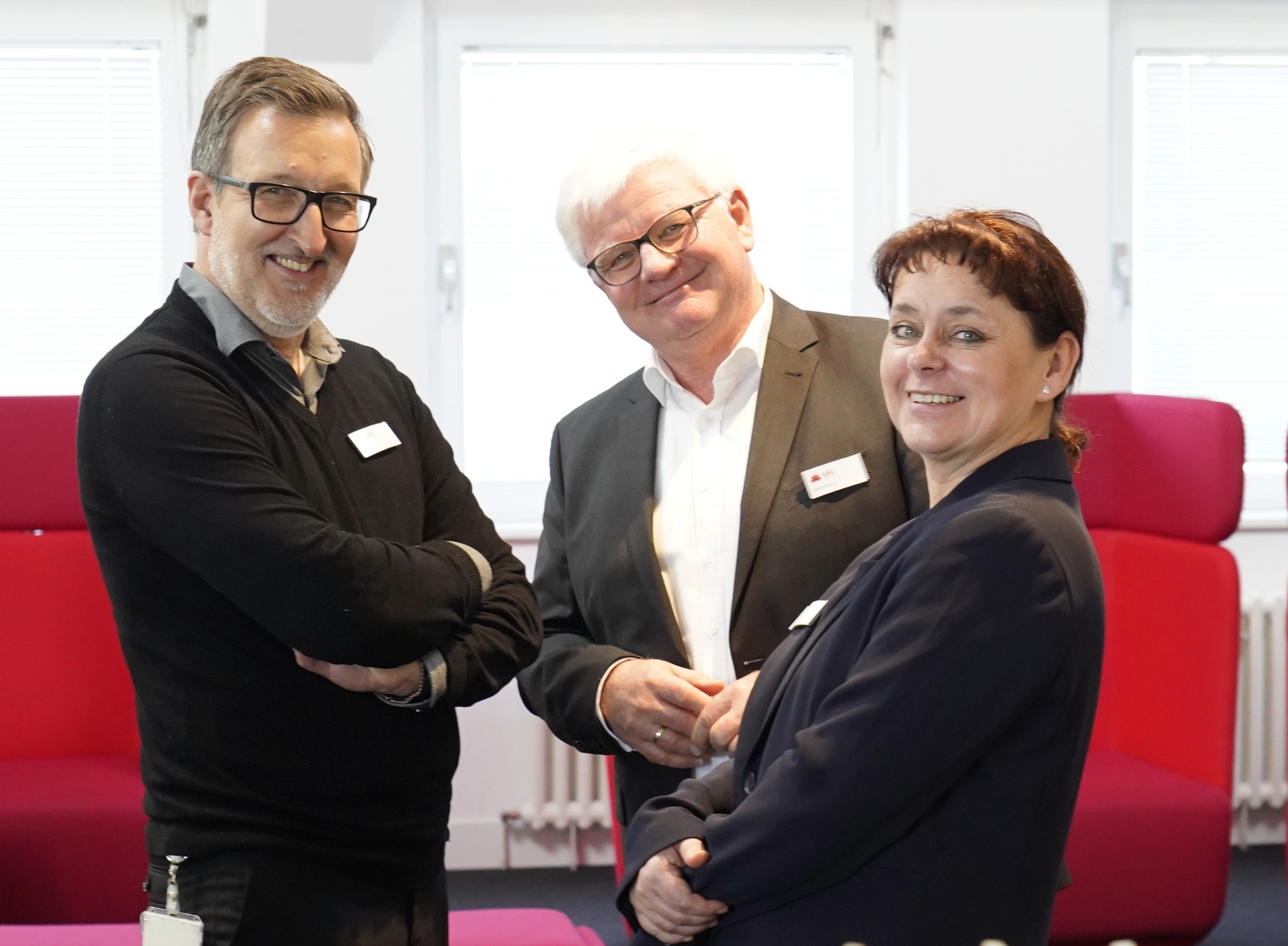 Drei GRG Mitarbeitende in formeller Kleidung, zwei Männer und eine Frau, lächeln in die Kamera